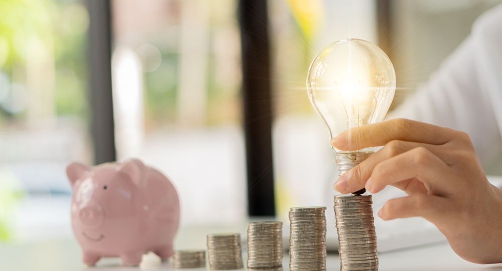 Businessman,Holding,A,Light,Bulb,On,A,Pile,Of,Silver