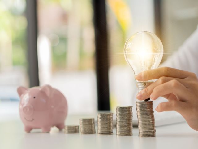 Businessman,Holding,A,Light,Bulb,On,A,Pile,Of,Silver