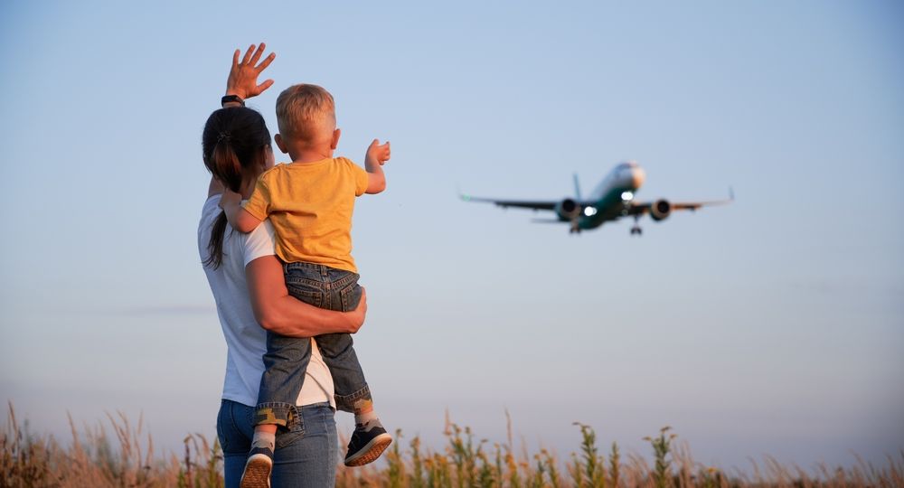 Back,View,Of,Woman,With,Child,Waving,Hands,To,Flying