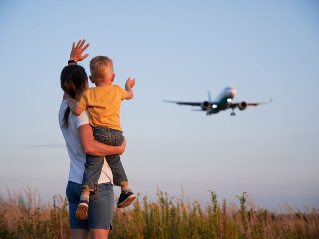 Back,View,Of,Woman,With,Child,Waving,Hands,To,Flying